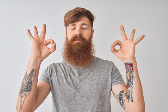 Young redhead irish man wearing t-shirt standing over isolated grey background relax and smiling with eyes closed doing meditation gesture with fingers. Yoga concept.