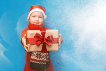 Little baby boy wear santa suit smile and show gift box with red bow on blue background. selected focus. christmas time