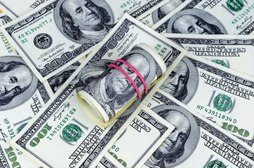 Roll of american dollars with red rubber lying on united states hundred dollar notes