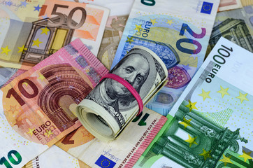Roll of american dollars with red rubber lying on euro banknotes of different nominal value