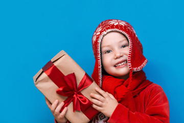 little boy in Santa's hat with cozy gift box and red tape want to know what inside the box, put to his ear