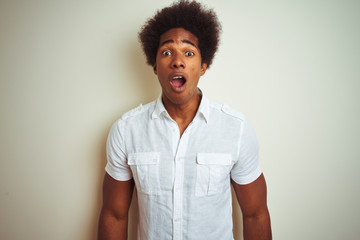 African american man with afro hair wearing shirt standing over isolated white background afraid and shocked with surprise expression, fear and excited face.