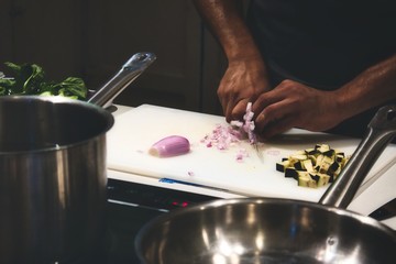 Close up of man's hands cutting onions on a chopping board in a professional kitchen