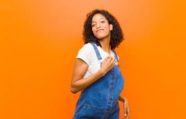young pretty black woman looking arrogant, successful, positive and proud, pointing to self against...