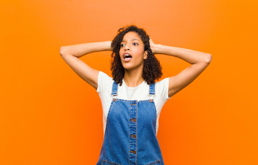 young pretty black woman with open mouth, looking horrified and shocked because of a terrible...