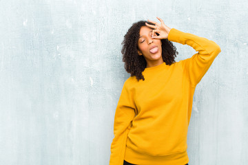 young pretty black woman smiling happily with funny face, joking and looking through peephole,...