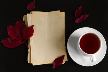 blank vintage paper sheets,red autumn leaves and hot tea cup flat lay on a black background