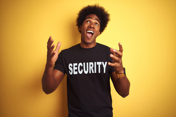 American safeguard man with afro hair wearing security uniform over isolated yellow background crazy and mad shouting and yelling with aggressive expression and arms raised. Frustration concept.