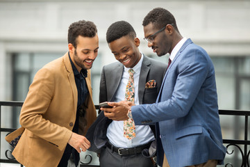 three handsome young men in suits near the building look at the phone