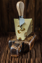 maasdam cheese on vintage cutting board and knife old dark wooden background