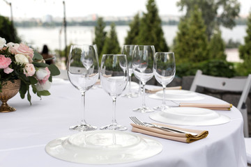 Wedding table setting decorated with fresh flowers in a brass vase. Wedding floristry. Banquet table for guests outdoors with a view of green nature. Bouquet with roses, eustoma and eucalyptus leaves