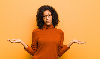 young pretty black woman feeling puzzled and confused, unsure about the correct answer or decision,...