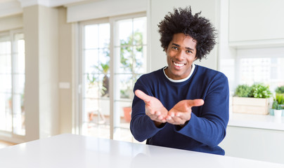 Young african american man wearing casual sweater sitting at home Smiling with hands palms together receiving or giving gesture. Hold and protection