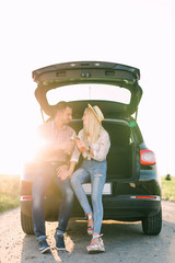 Beautiful young couple sitting drink cold drinks in car trunk