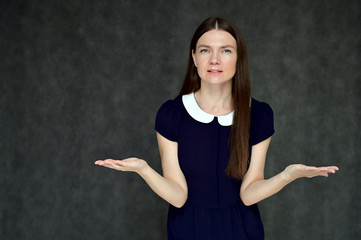 Portrait of a pretty young brunette woman with combed hair on a gray background in a dark blue dress. It is in different poses. Looks straight at the camera. Slim figure.