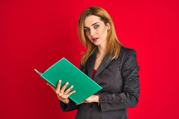 Young beautiful redhead businesswoman wearing suit reading book