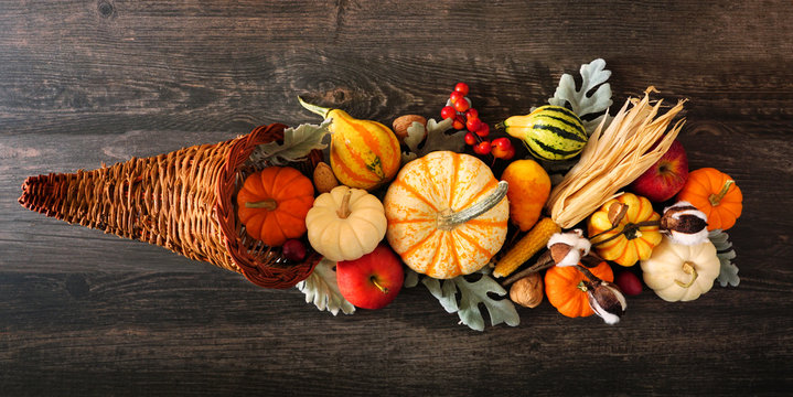 Thanksgiving cornucopia filled with autumn vegetables and pumpkins. Above view against a dark wood background.