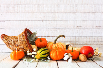 Thanksgiving cornucopia filled with autumn vegetables and pumpkins against a rustic white wood...