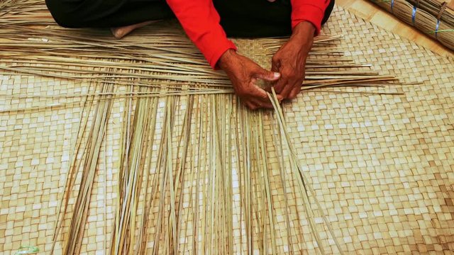 Close up shot of an expert old female hands weaving mat in Terengganu, Malaysia. The mat which is made from natural plant leaves come in various colors and sizes.