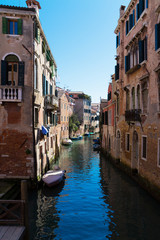 Fototapeta na wymiar Old narrow canal with parked boats, Venice, Italy. Traditional flooded street or alley of Venice. Vertical view.