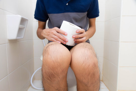 Young man sitting in the toilet with holding tissue
