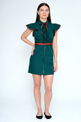 Vertical Full-length portrait of a pretty young brunette woman with combed hair on a white background in a green dress. It is in different poses. Looks straight at the camera. Slim figure.