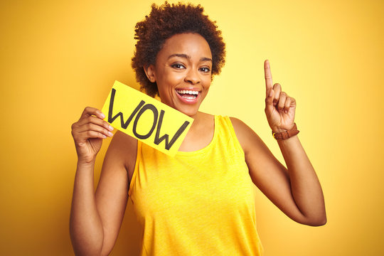 Young african american woman showing wow banner board over yellow isolated background surprised with an idea or question pointing finger with happy face, number one