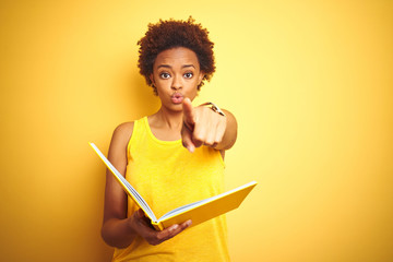 African american woman reading a book over yellow isolated background pointing with finger to the...