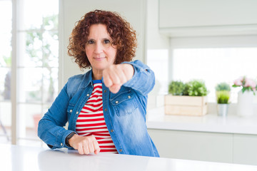 Middle age senior woman with curly hair wearing denim jacket at home Punching fist to fight, aggressive and angry attack, threat and violence