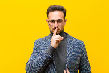 young handsome man looking serious and cross with finger pressed to lips demanding silence or...