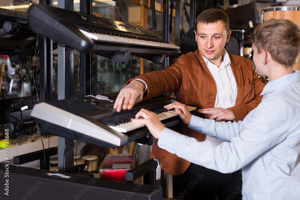 Wall mural Father and teenage son examining keyboards in guitar shop