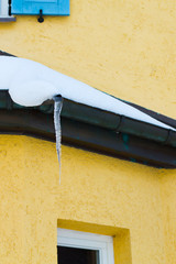 Icicles and snow on an old yellow house, vertical