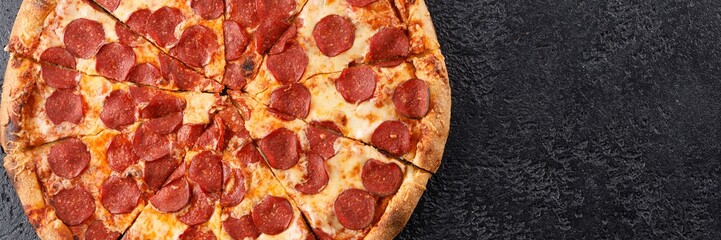 Traditional piperoni pizza on a black textural background. Close-up. The concept of delicious food. Top view.