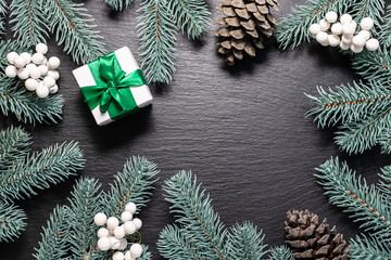 Christmas and New Year greeting card template with fir tree, gift box, pine cones and decor on black stone background.