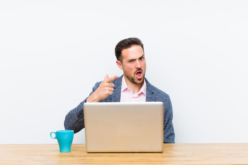 young handsome businessman pointing at camera with an angry aggressive expression looking like a...