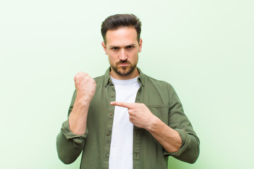 young handsome man looking impatient and angry, pointing at watch, asking for punctuality, wants to...