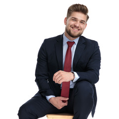 excited young businessman holding tie and sitting in studio