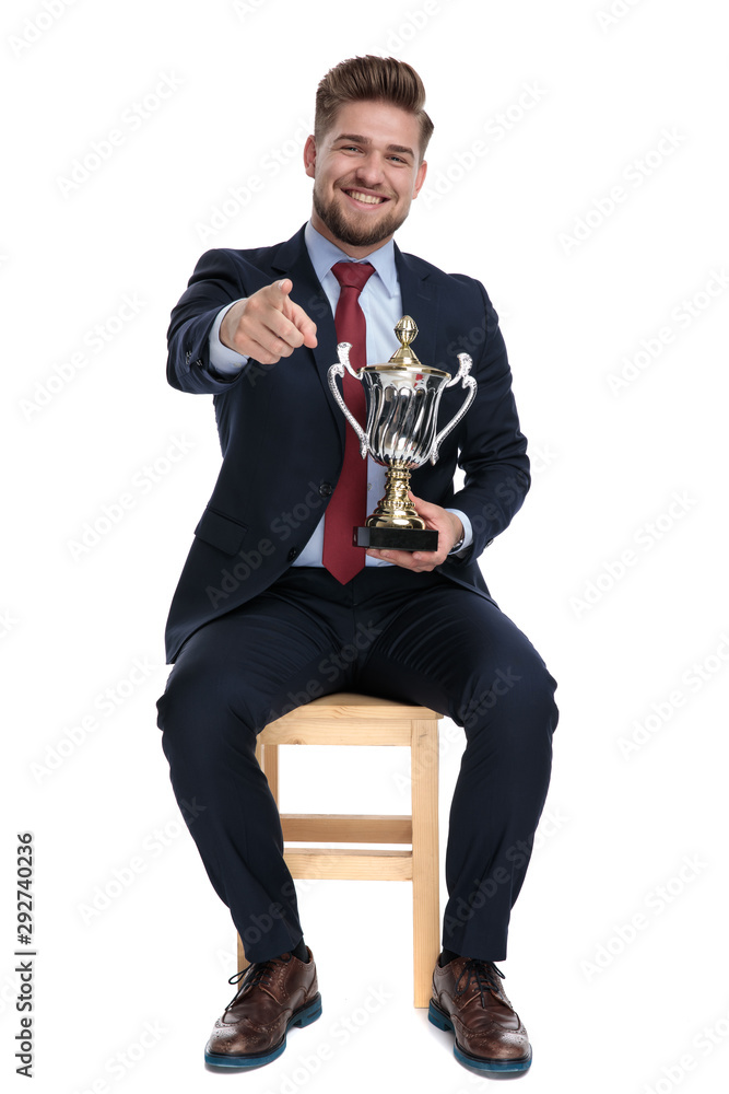 Wall mural excited young businessman holding trophy and pointing finger