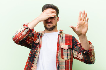young handsome man covering face with hand and putting other hand up front to stop camera, refusing...