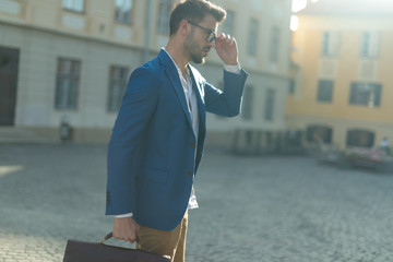 attractive young man fixing glasses outdoor in an urban scene