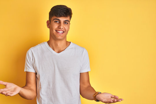 Young indian man wearing white t-shirt standing over isolated yellow background smiling cheerful with open arms as friendly welcome, positive and confident greetings
