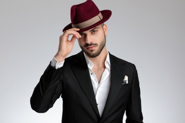 businessman standing and fixing his hat while looking at camera