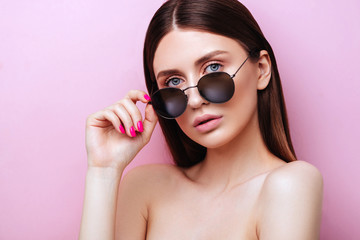 Portrait of an attractive young girl in round glasses on a pink background in studio