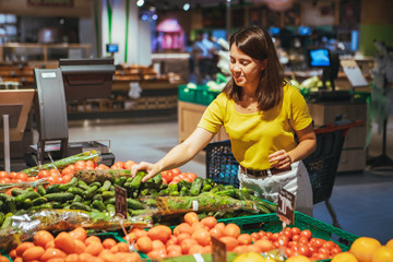woman choosing cucumber from store shelf grocery shopping