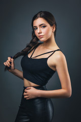 Portrait of a young beautiful brunette of athletic build. Model posing in black clothes on a dark background.