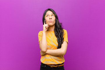 young pretty latin woman with a concentrated look, wondering with a doubtful expression, looking up...