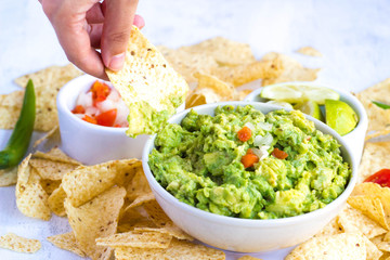 Guacamole with pico de gallo. Hand eating a nacho. Delicious healthy avocado food concept, on a white background