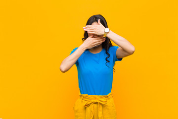 young pretty latin woman covering face with both hands saying no to the camera! refusing pictures...
