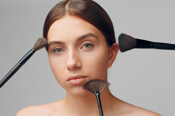 Beautiful woman face with natural makeup. Hand of make-up master with brush. Young beauty model...