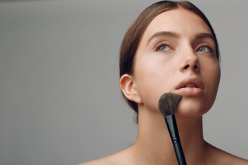 Beautiful woman face with natural makeup. Hand of make-up master with brush. Young beauty model...